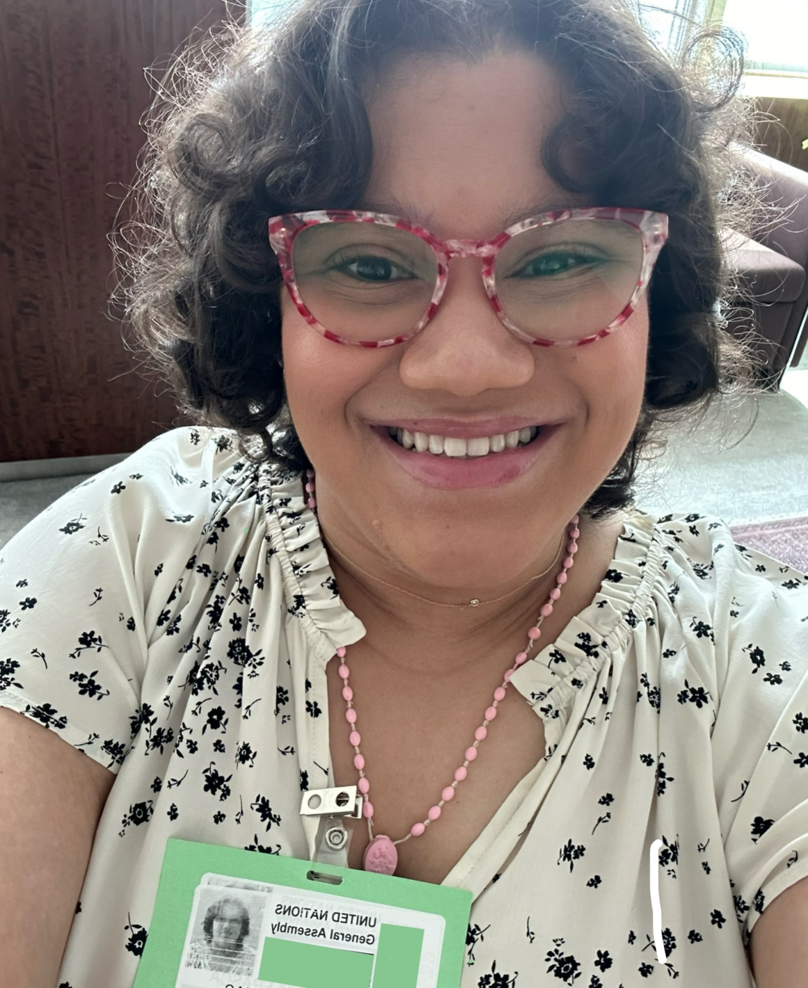 young hispanic woman with dark curly hair and red and white glasses wearing a white shirt with black flowers