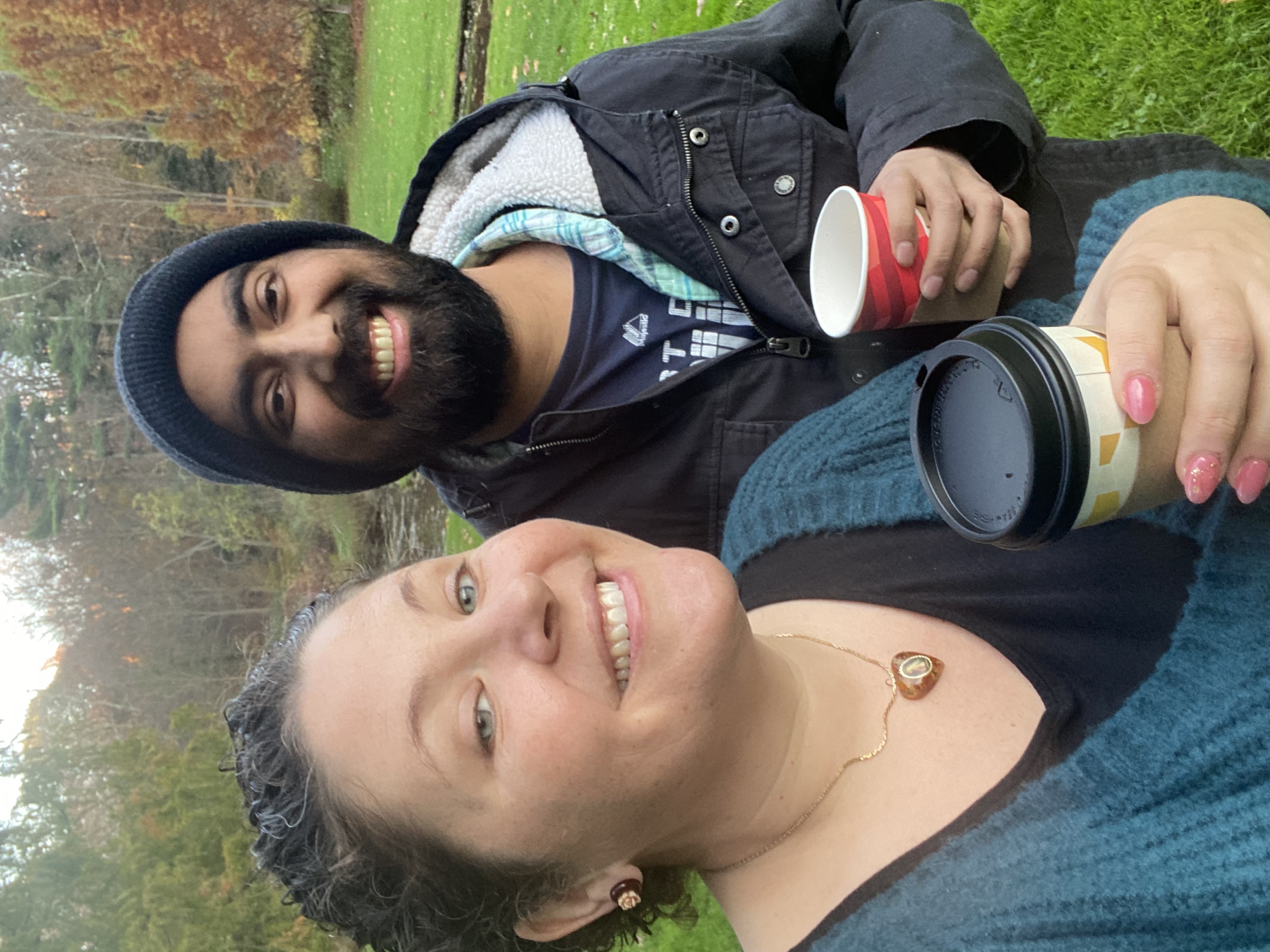 young white woman in blue sweater holding coffee with young black man with beard and mustanche wearing a knit cap and blue jacket holding a cup