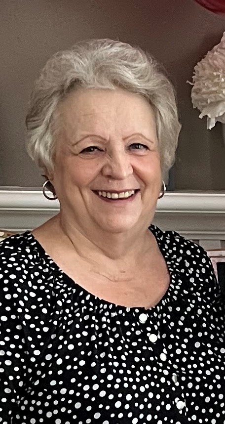 older white woman with short white hair wearing silver hoop earrings and a black and white polka dot blouse