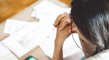 Woman with head in hands looking down at bills