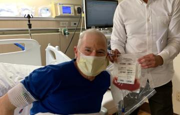 Man in blue shirt and mask in a hospital bed with a medical worker holding a bag of stem cells