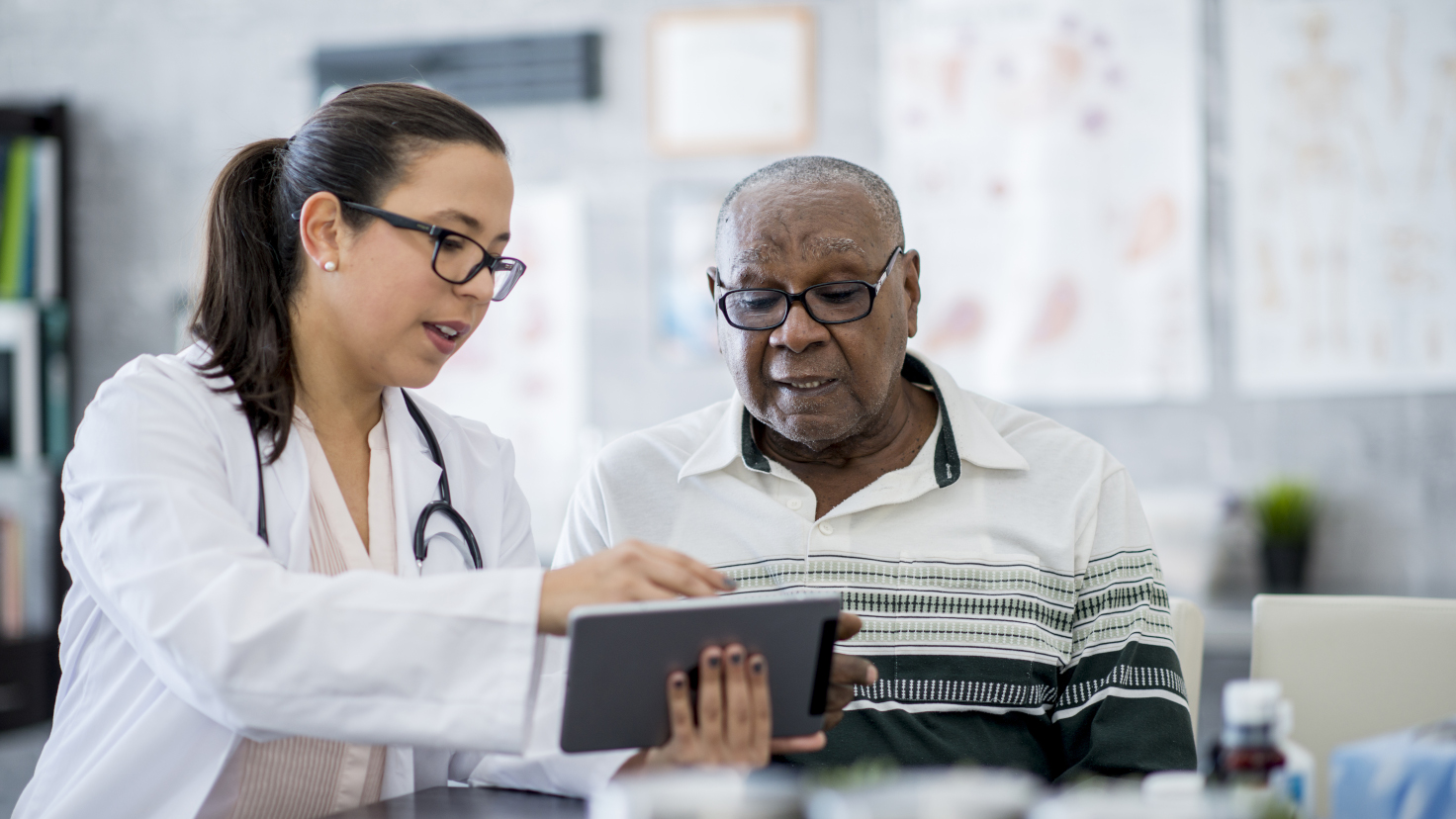 Doctor in white lab coat looking at tablet with patient