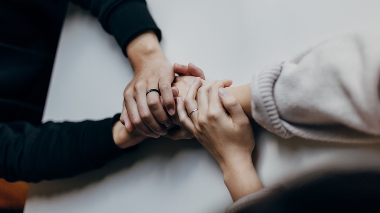 Two sets of light-skinned hands holding each other across a table.