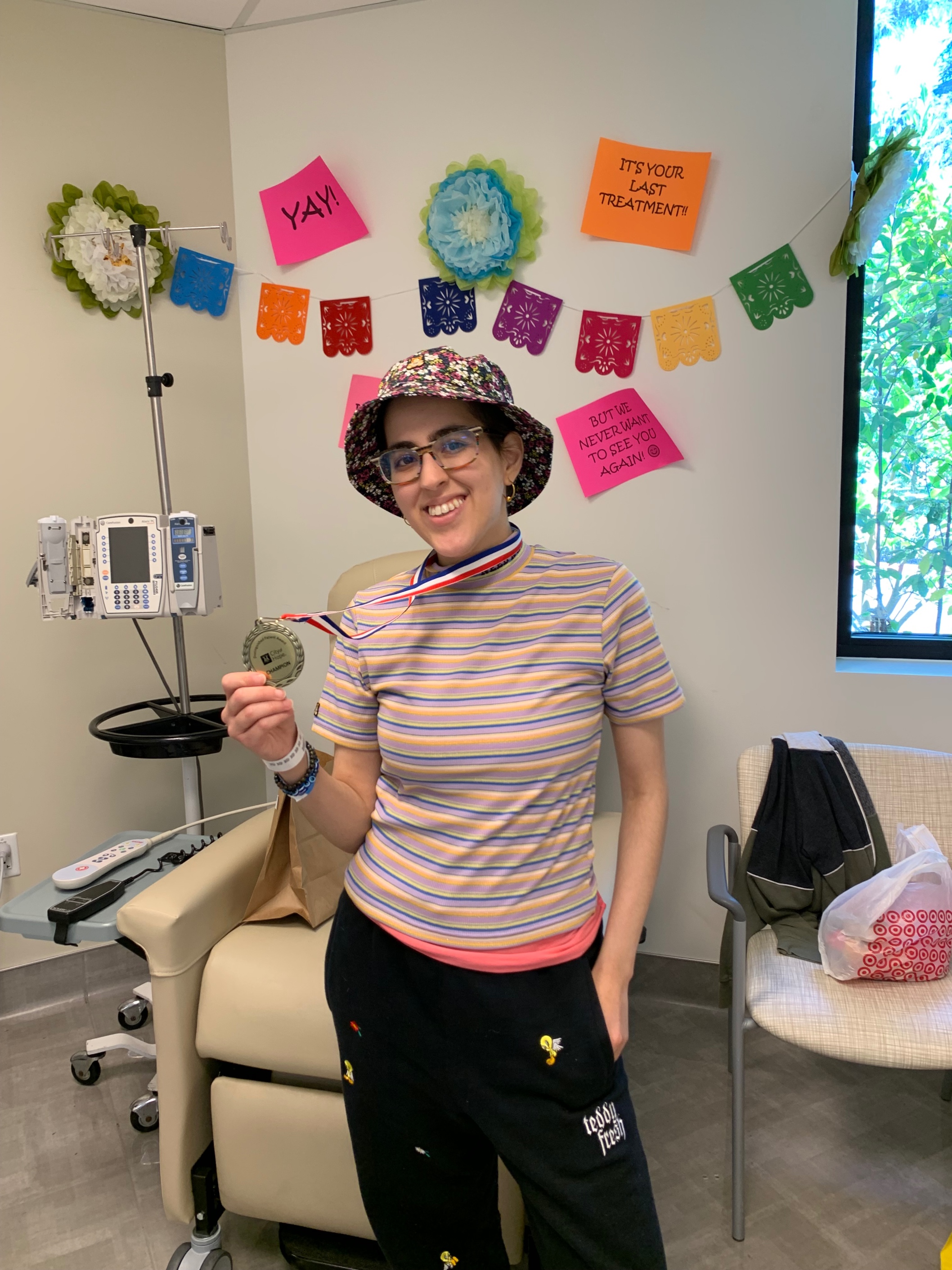 Young woman with glasses wearing a floral bucket hat holding a medal in her hand striped shirt and sweatpants