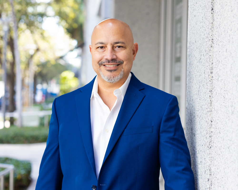 balding middle aged hispanic man with graying beard and mustache smiling and wearing a royal blue jacket and white shirt