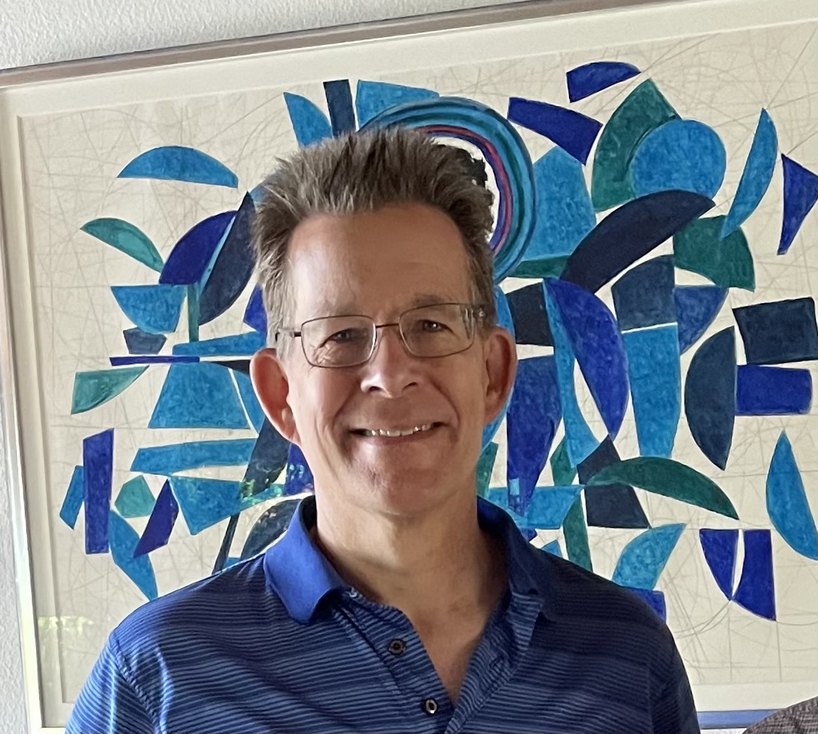 older white man with spiky hair wearing glasses and a blue striped shirt in front of mosaic artwork