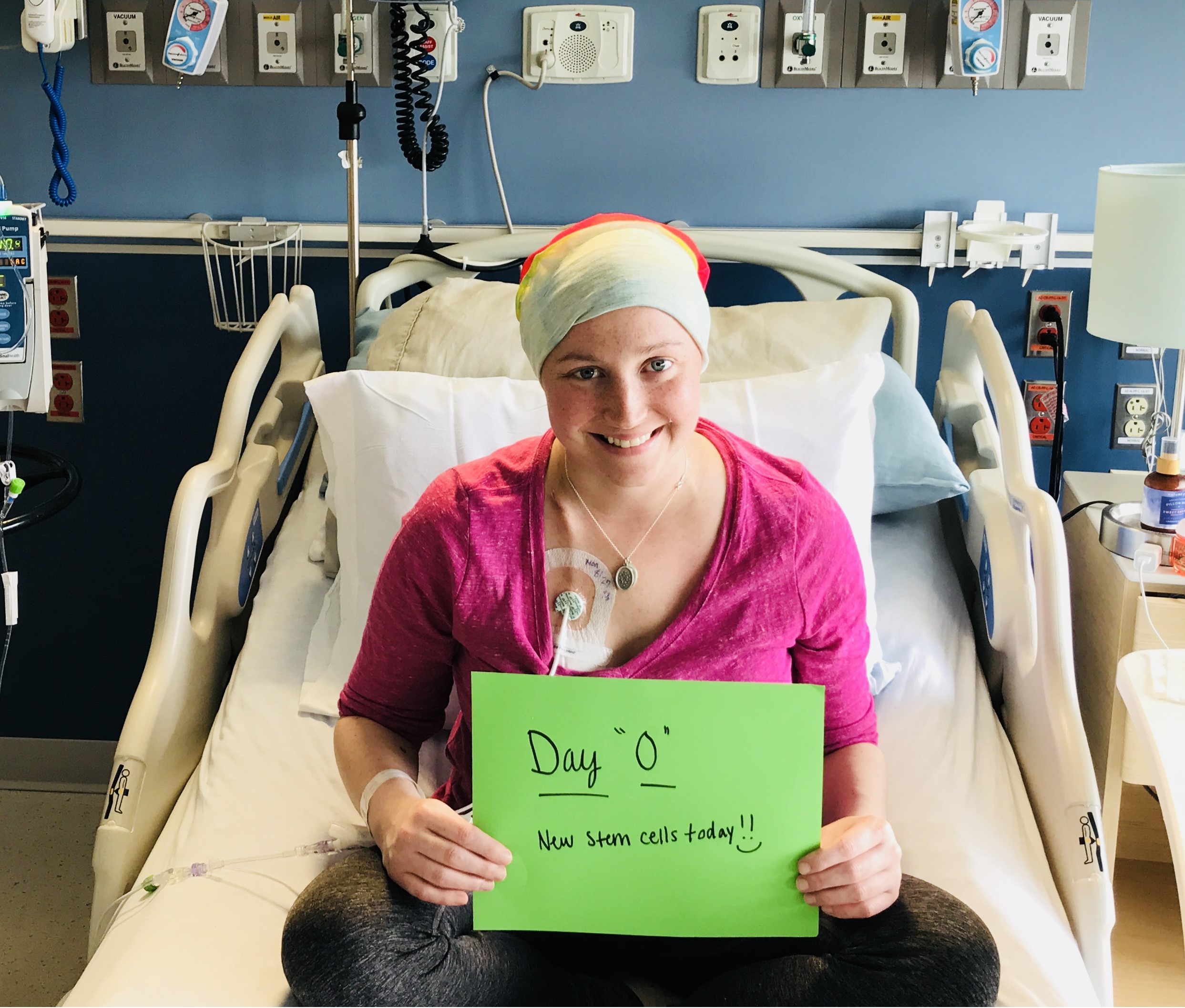 young white woman in a hospital bed wearing a pink shirt, turban and holding a green sign that says new stem cells today