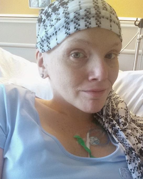 young white woman with a scarf on her bald head wearing a blue shirt laying in a hospital bed