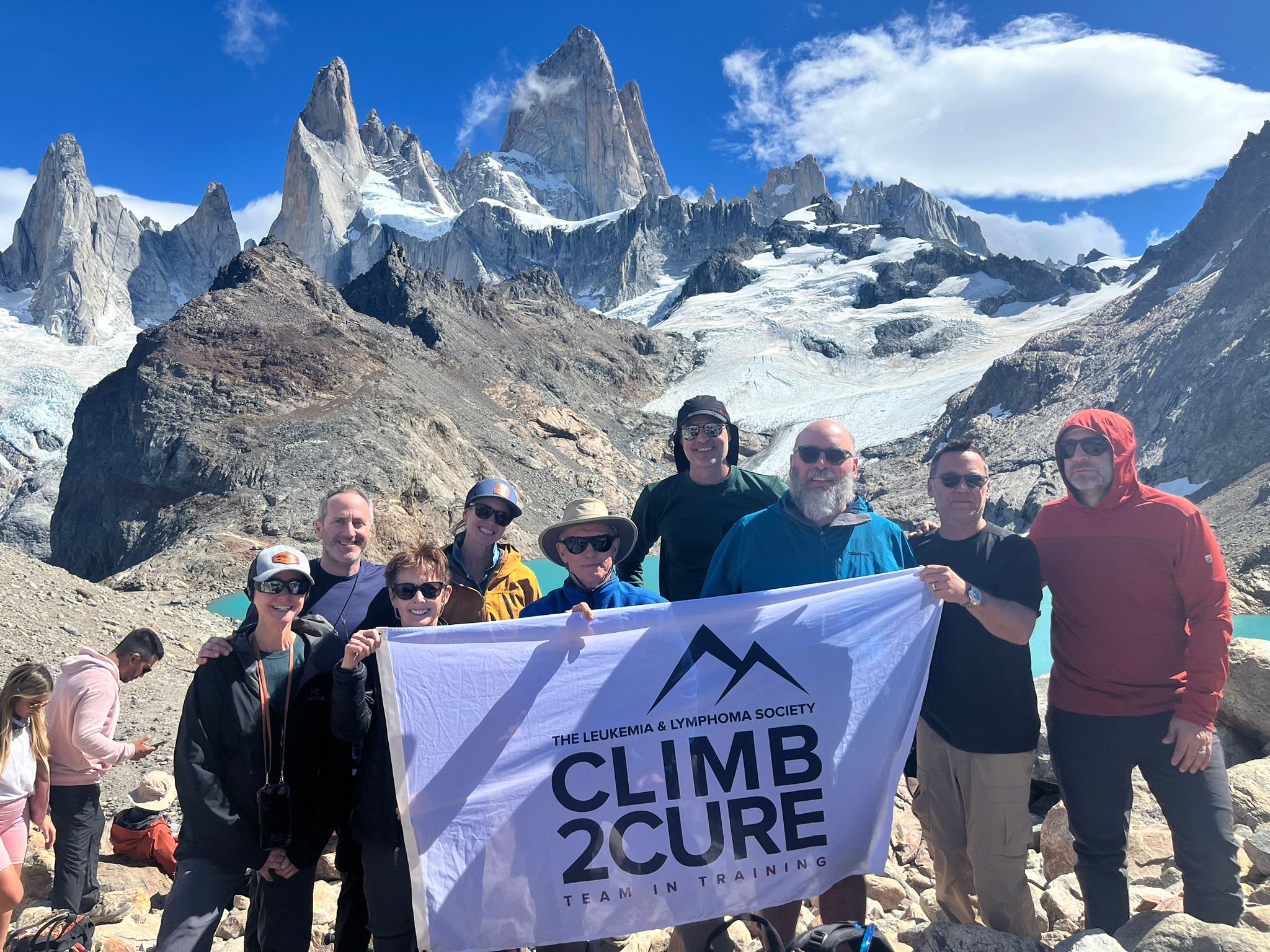 a group of nine people standing at the top of a mountain holding a Climb2Cure banner