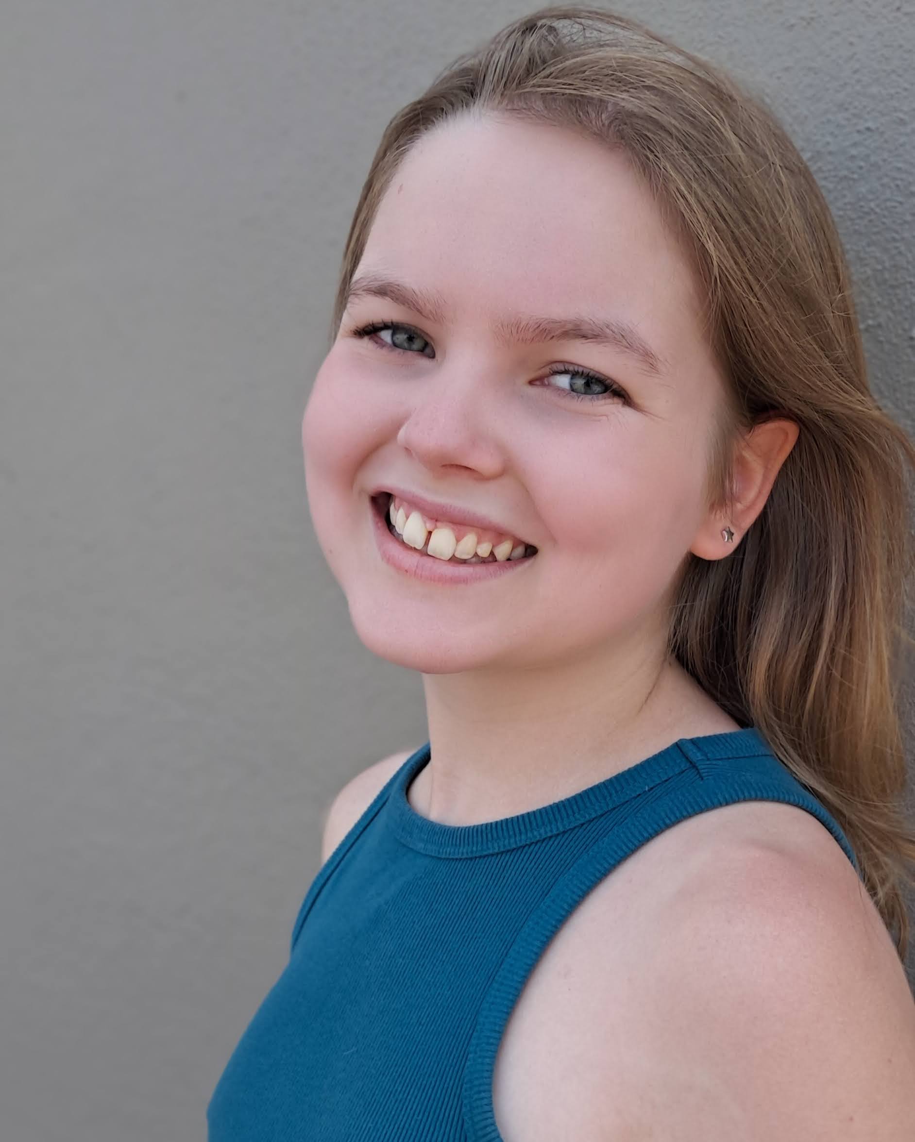 young white girl with brown hair and star earrings with a slight gap in her two front teeth wearing a blue tank top