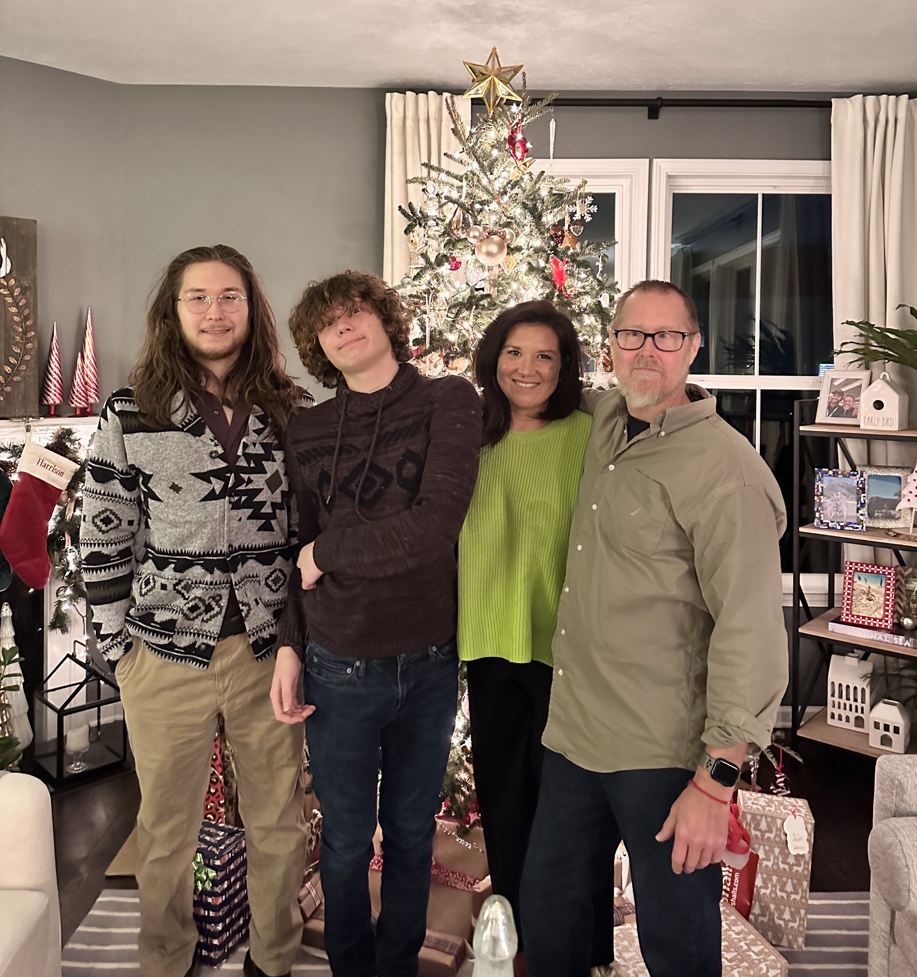 John William middle aged white man wearing glasses and a gray shirt standing in front of Christmas tree with his wife in a green sweater and two sons