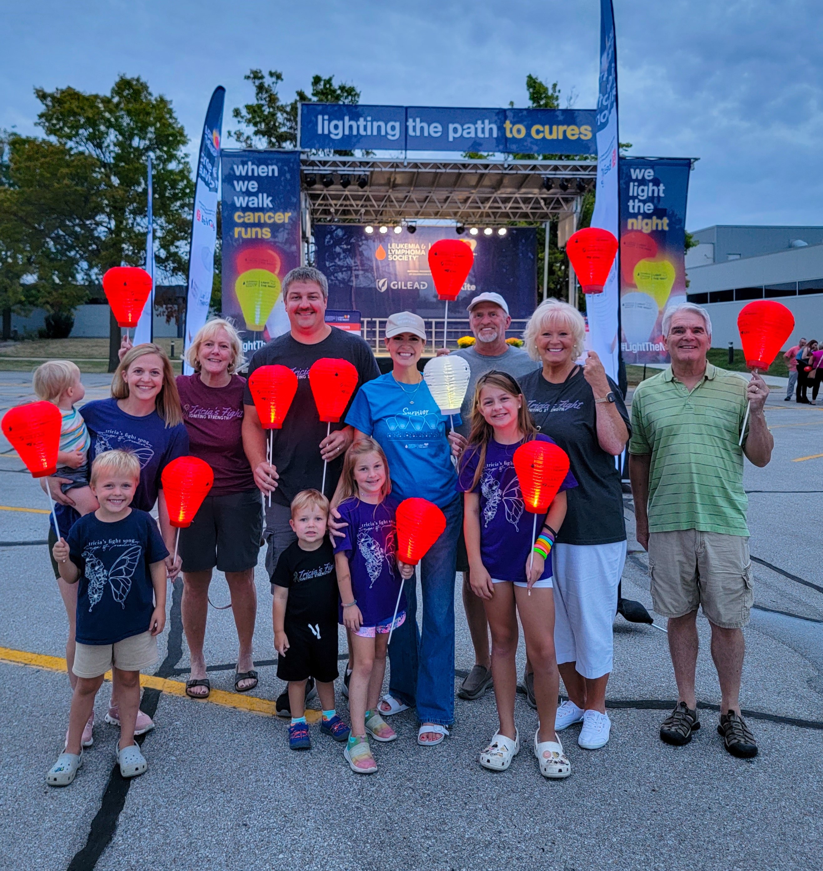 Tricia young white woman wearing a khaki ball cap and blue t-shirt and jeans holding a white LTN balloon surrounded by adutls and children holding orange balloon at a LTN walk