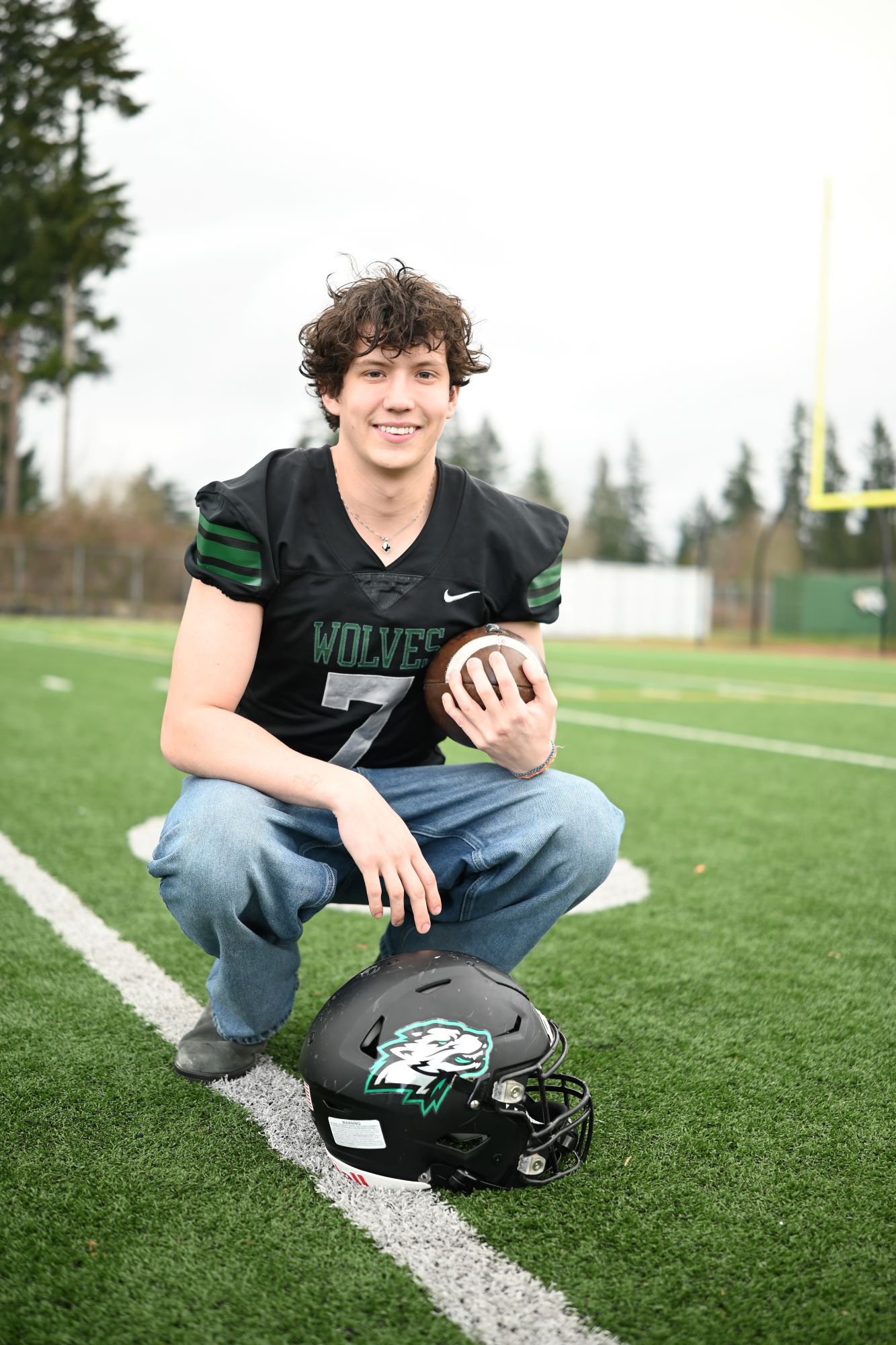 young adult smiling while holding a football on the field wearing a jersey