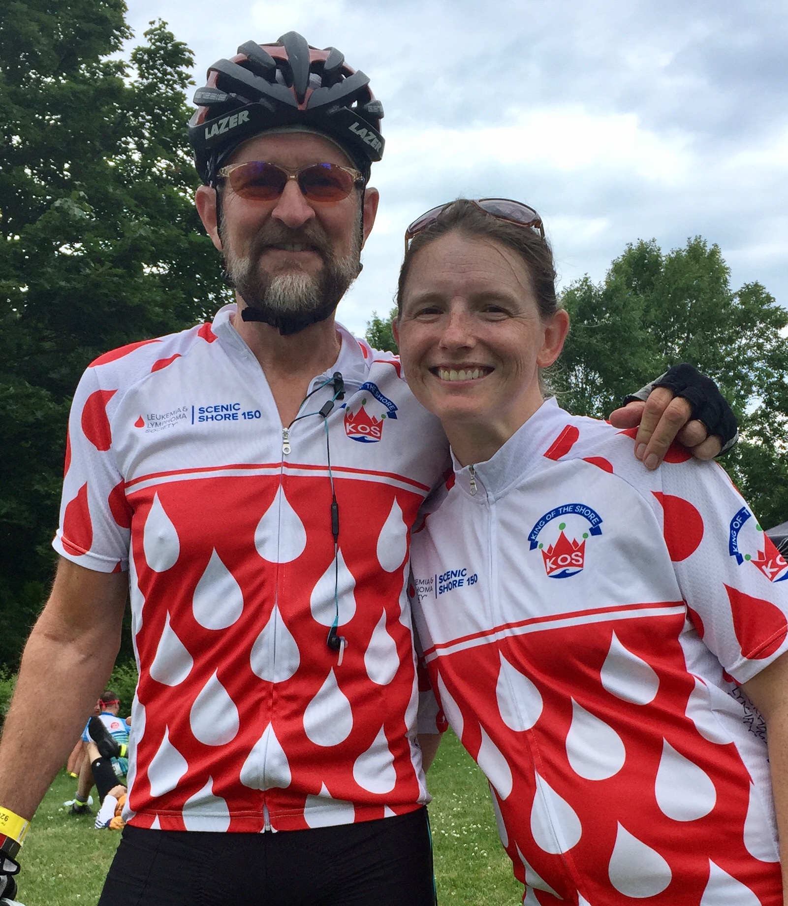 Paul older white gentleman with beard and mustache wearing a bike helmet and sunglasses with younger white female with freckles and sunglasses on her head both wearing Scenic Shore 150 shirts