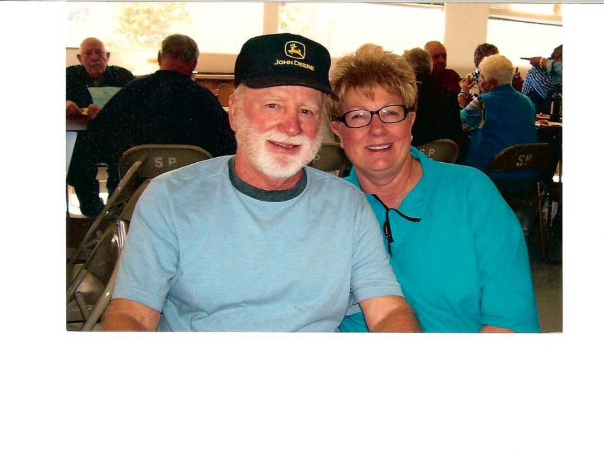 Ron older white man with white beard and mustache wearing John Deere hat and blue tshirt with wife with short hair glasses and turquoise shirt