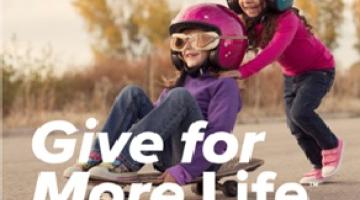 Two children wearing helmets and riding on a skateboard