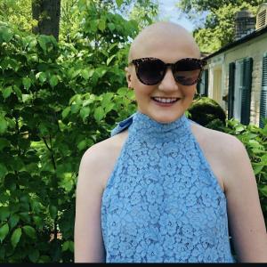 Bald white young lady wearing sunglasses and a blue top