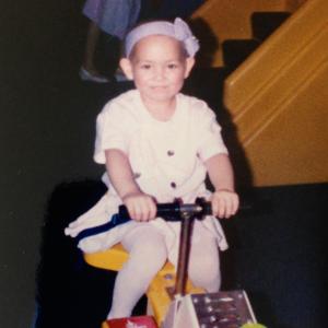 Little girl with leukemia on a scooter with a purple ribbon headband