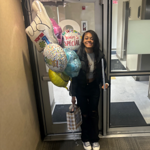 Young black woman in black jacket and pants holding mylar balloons