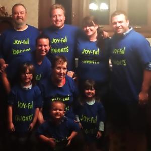 Six adults and three children all wearing blue shirts that say Joy-ful Nights