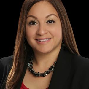 Young hispanic woman with long brown hair in a red top and black jacket wearing a necklace and earrings