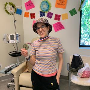 Young woman with glasses wearing a floral bucket hat holding a medal in her hand striped shirt and sweatpants