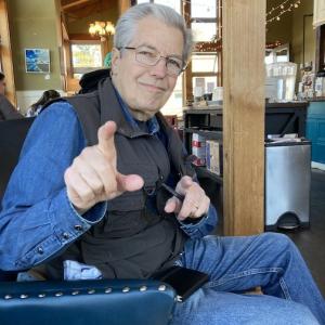 Older white man wearing glasses a denim shirt with a black vest and jeans pointing a finger.jpg