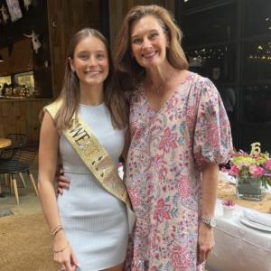 young white woman wearing sweet sixteen sash and white dress with cowboy boots and her mother in a floral dress and sneakers