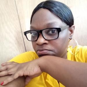 black woman with her hair pulled back wearing black glasses and a yellow shirt resting her chin on her arm