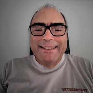 middle aged balding hispanic man with bushy eyebrows wearing black glasses and an Oktoberfest t-shirt