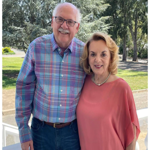 older white balding man with glasses and blue plaid shirt with older white woman with blond hair necklace and pink blouse