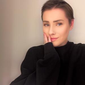 young white woman with short hair and a nose ring wearing a black sweater hand on her face