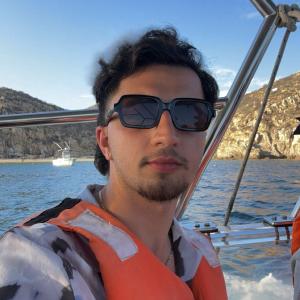Steven young white male with dark hair and light mustache and beard wearing sunglasses and life vest over white and black shirt standing on a boat