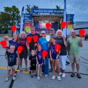 Tricia young white woman wearing a khaki ball cap and blue t-shirt and jeans holding a white LTN balloon surrounded by adutls and children holding orange balloon at a LTN walk