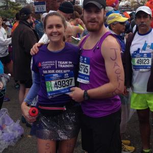 young white woman in a TNT shirt and race number and a sequined skirt with survivor written on her leg standing next to young white man with a black Nike hat beard and mustache
