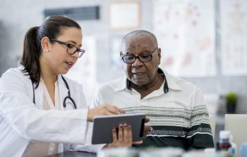 Doctor in white lab coat looking at tablet with patient