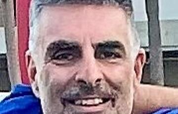 middle aged white man with graying beard and mustache with something blue around his neck