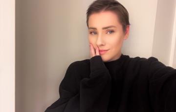 young white woman with short hair and a nose ring wearing a black sweater hand on her face