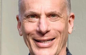 Geoff older white man with graying hair smiling and wearing a blue checked shirt