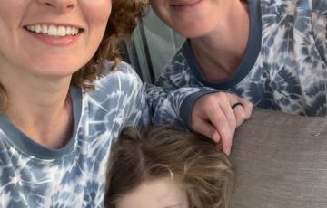 Kimbery two young white women and a little girl all wearing blue tie-dye shirts sitting on a brown sofa